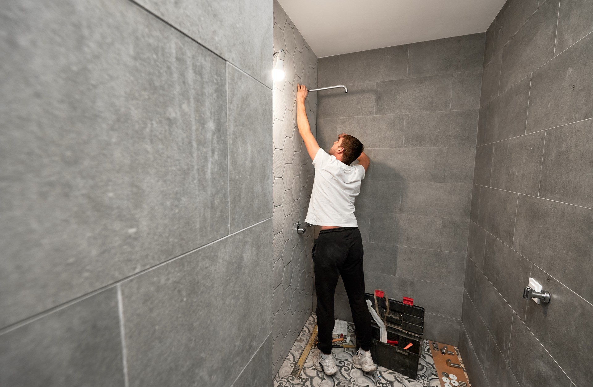 Male plumber installing shower head in bathroom.